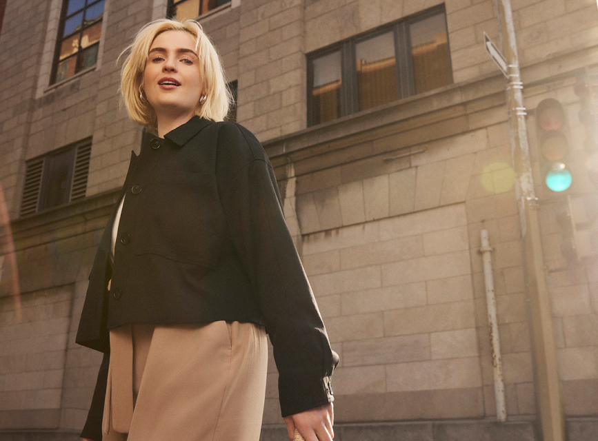 A blonde woman in a black jacket crossing the street.