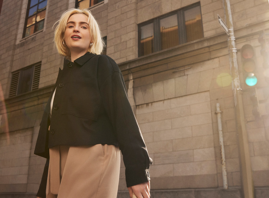 Une femme blonde vêtue d'une veste noire traverse la rue.