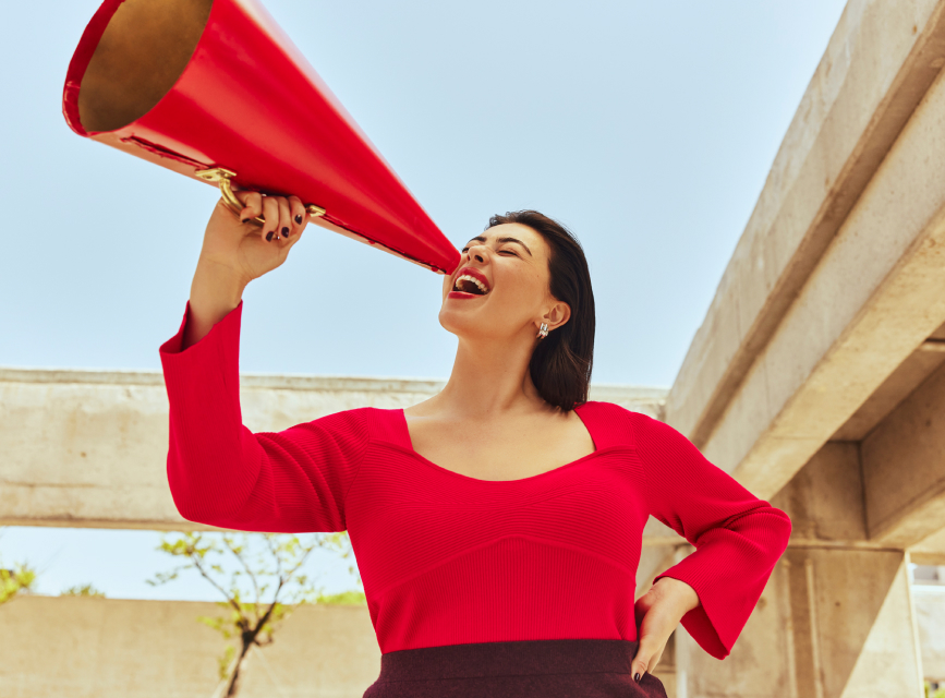 A woman in a red top shouting through a red loudspeaker.