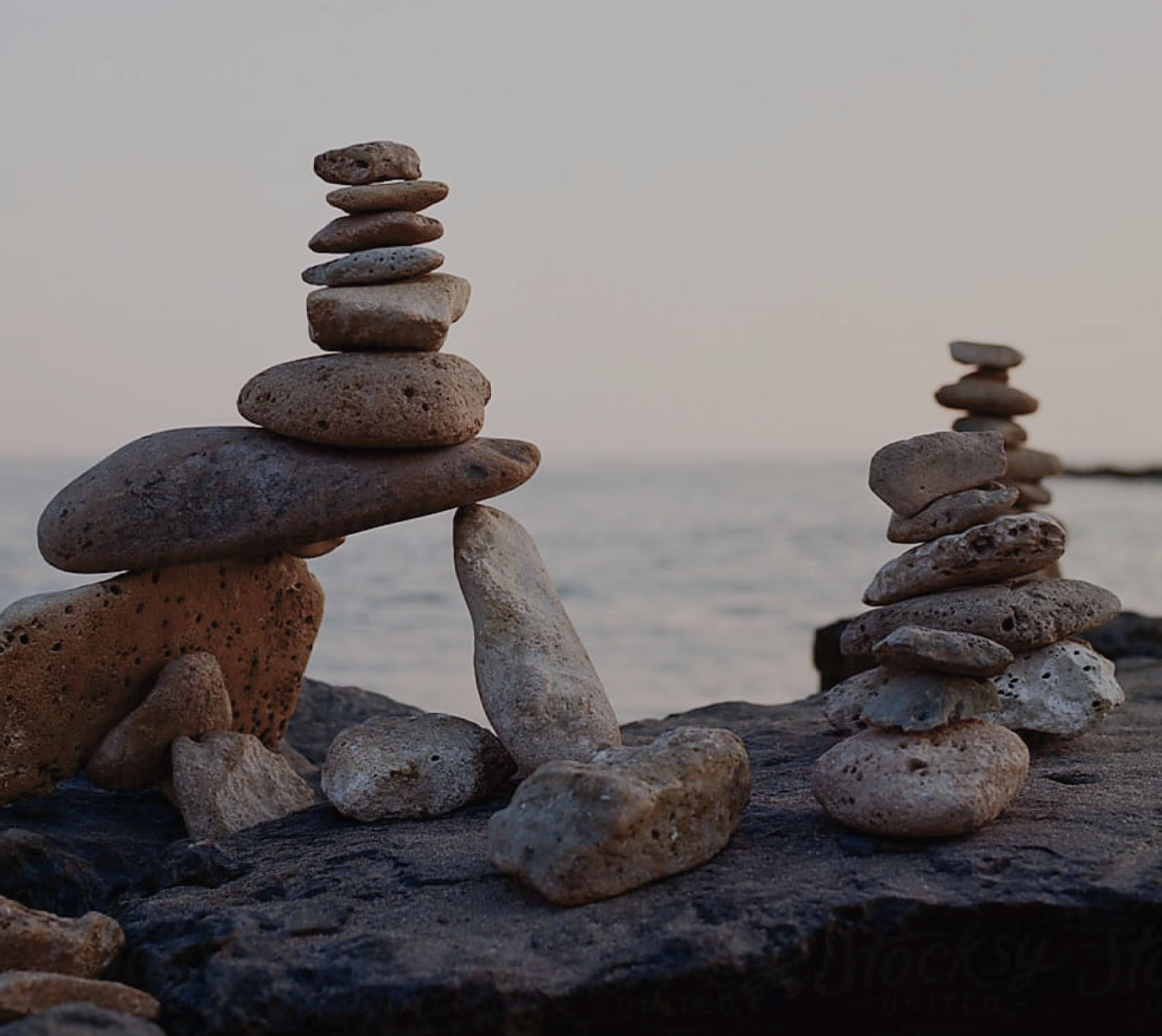 Two cairns of stacked stones standing by the water.