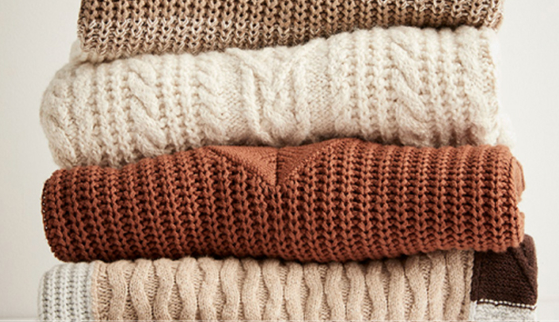 A stack of knit sweaters in neutral colours.