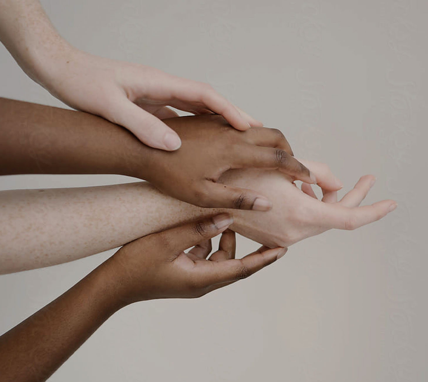 Four hands with diverse skin tones reach together.